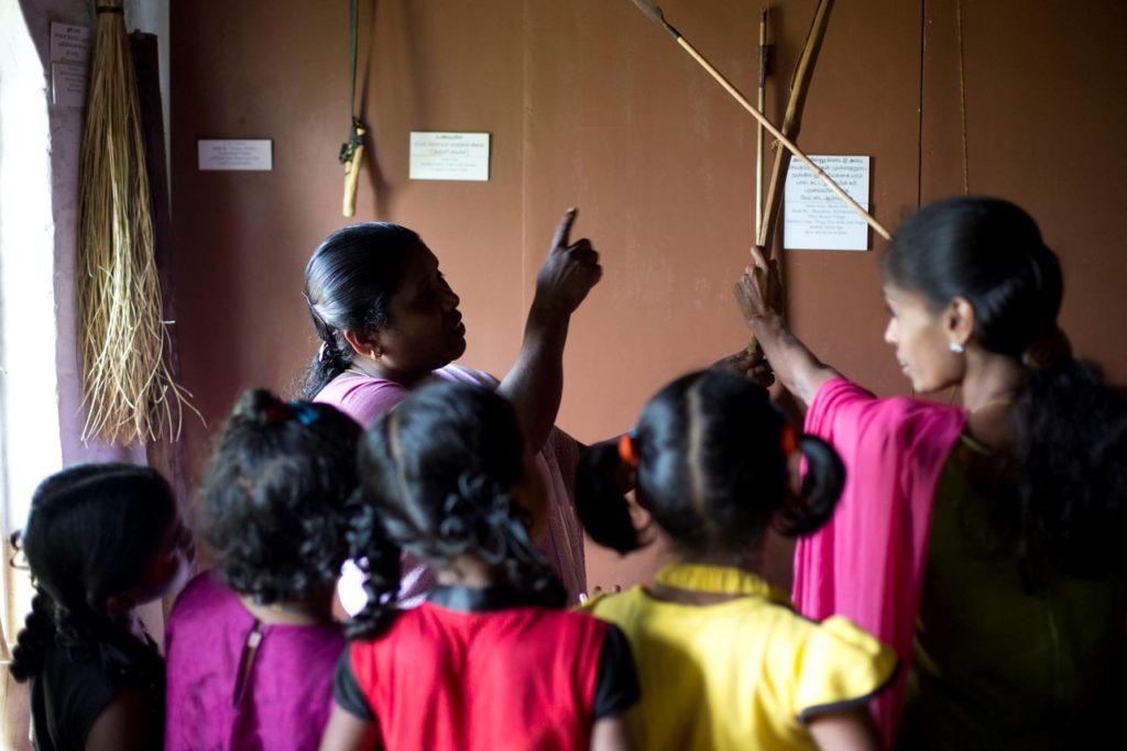 An elder shows children traditional Adivasi tools, labelled in their own language
